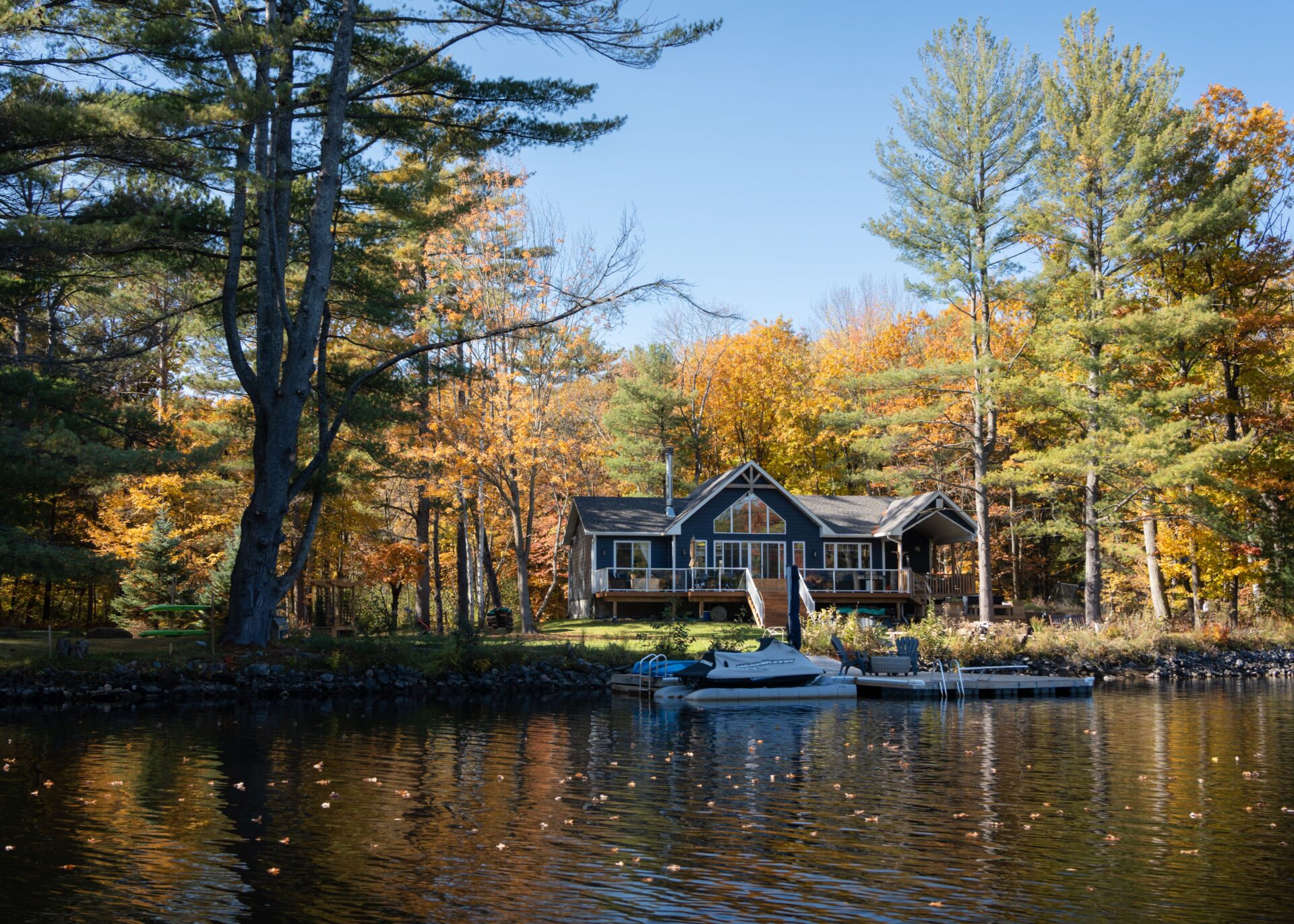 A beautiful autumn scene of a riverside cottage on the Muskoka River surrounded by a vibrant forest