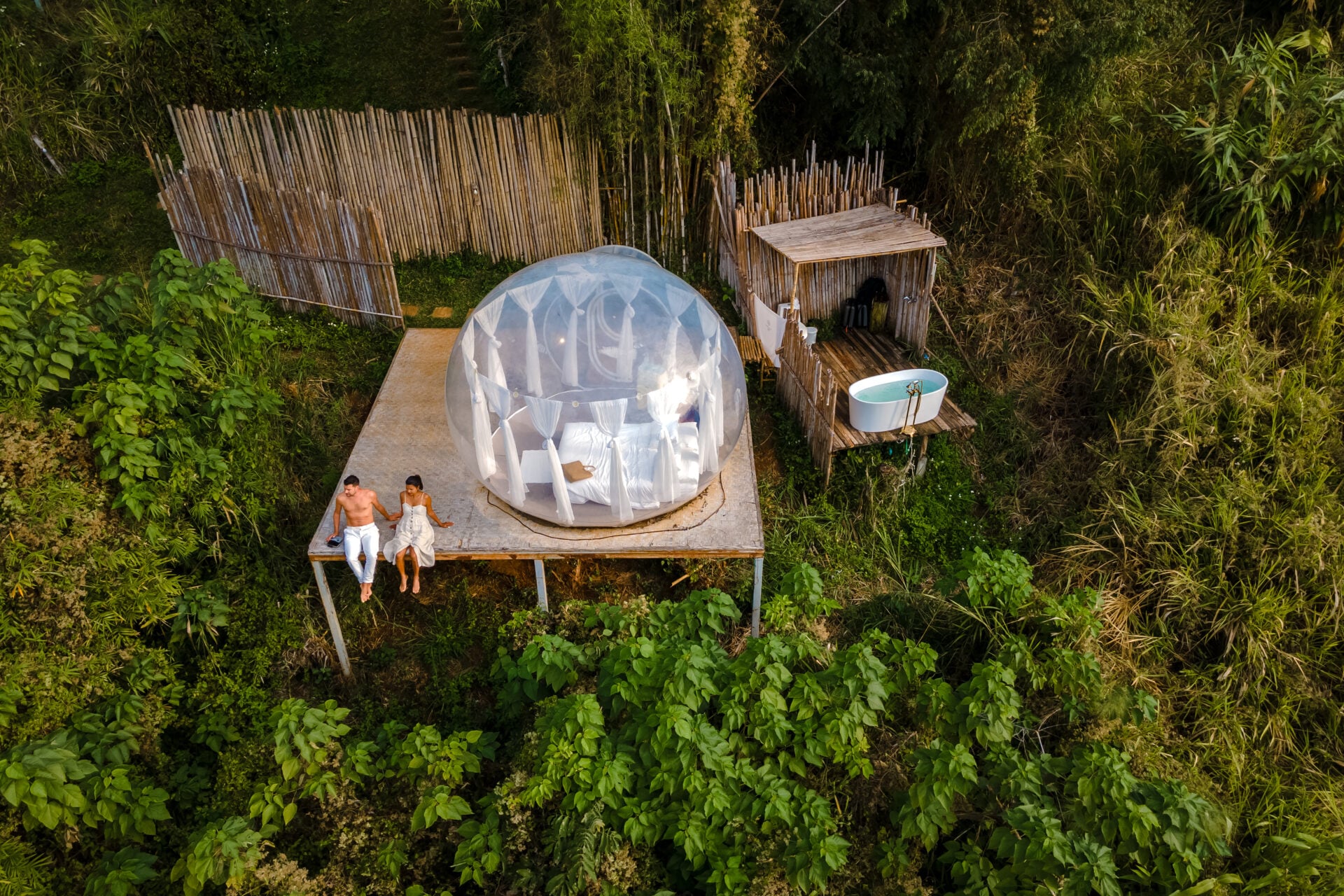 couple man and women in a bubble tent with an outdoor bathroom with a bath in the jungle rainforest. Luxury glamping