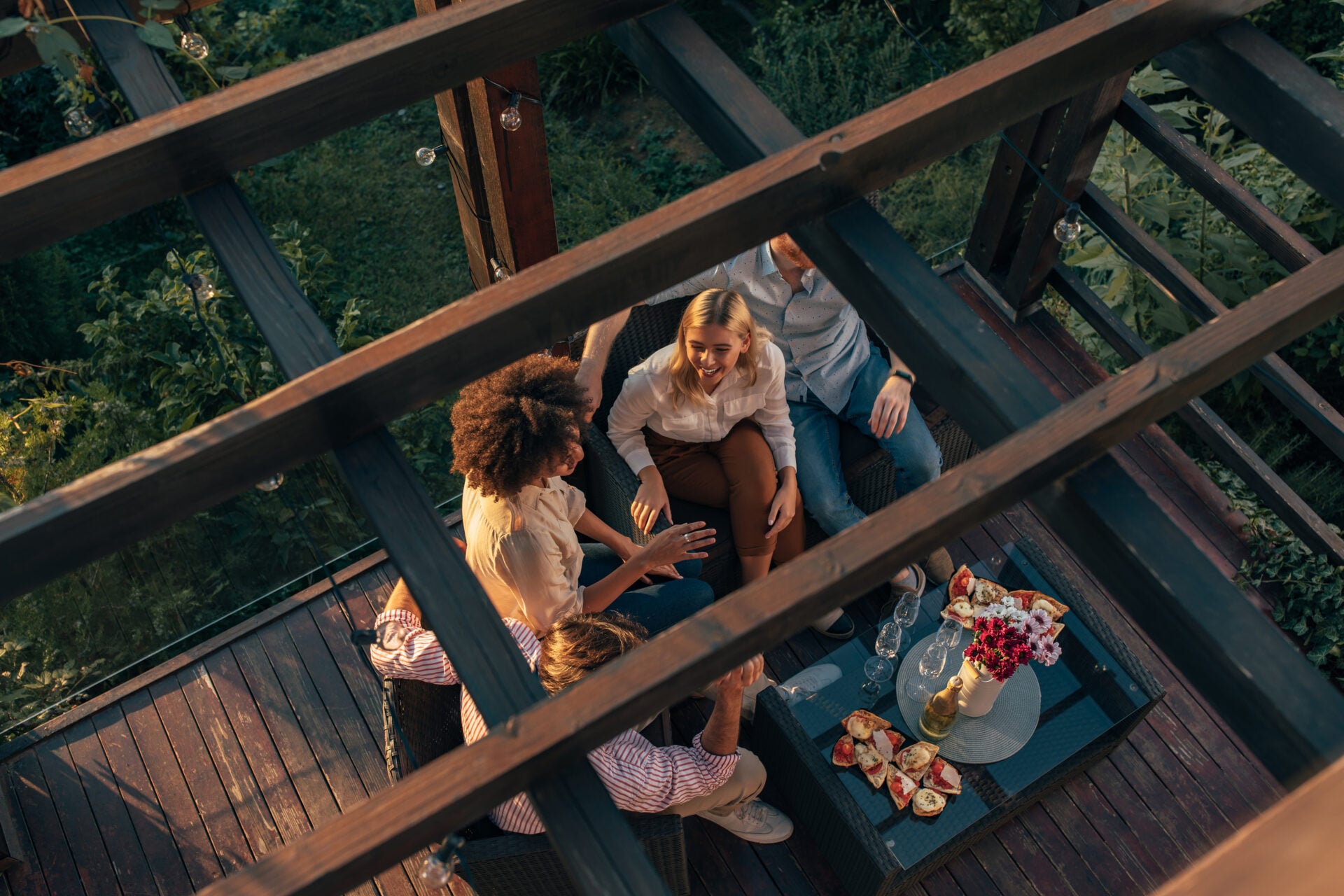 Two young couples sitting together on the terrace and socializing during beautiful sunset. View from above