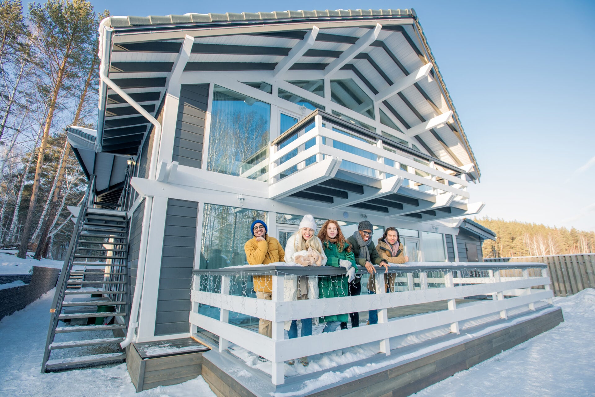 Horizontal group shot of young men and women wearing casual winter clothes standing on porch looking at camera smiling
