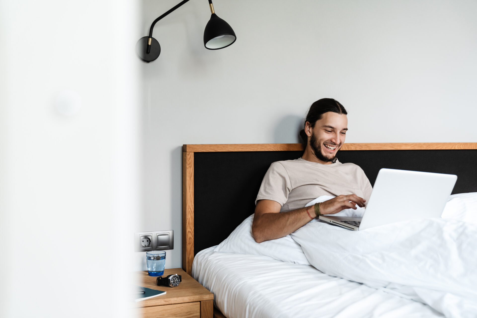 Happy man working on his laptop in his bedroom in the morning
