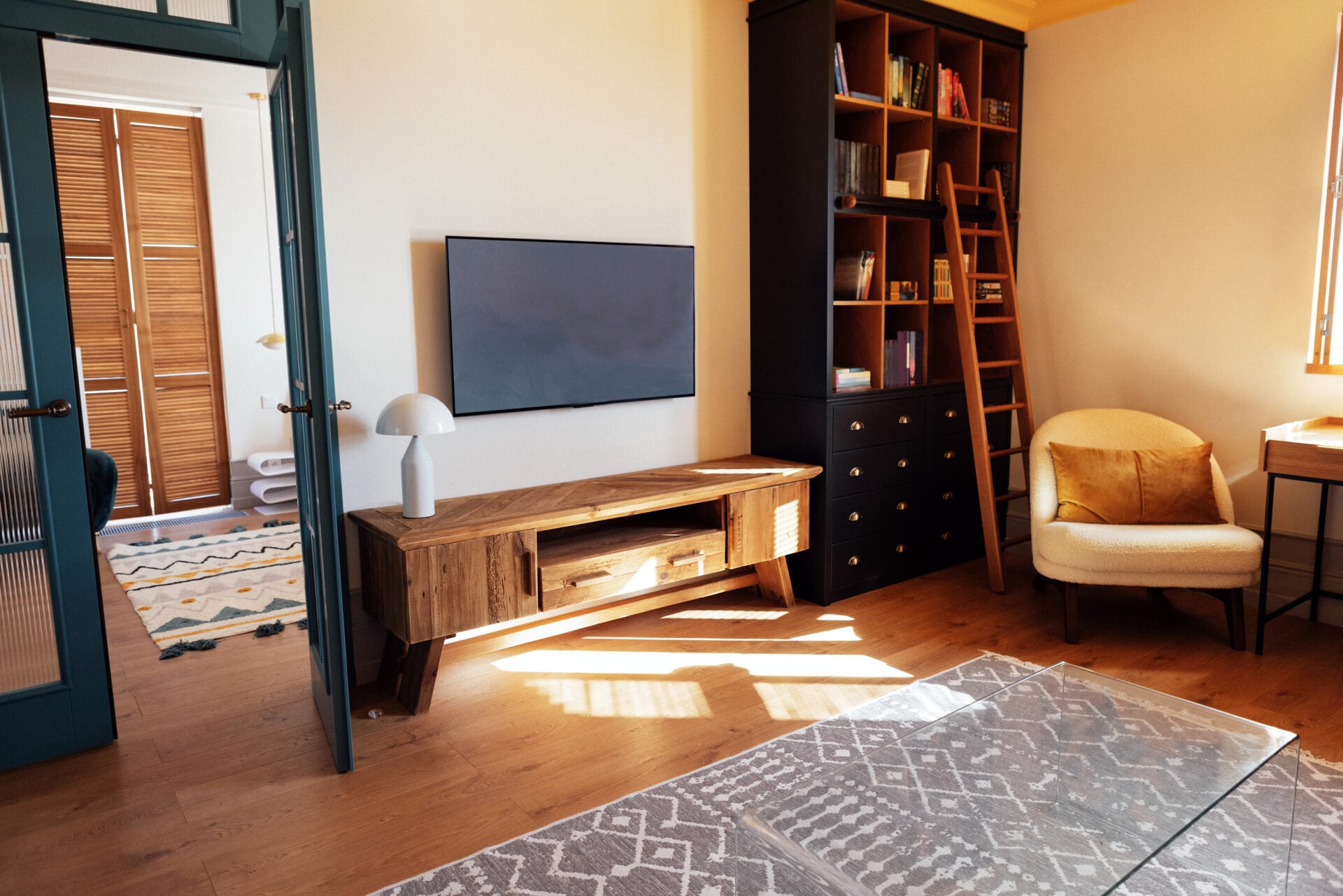 Close-up details of an elegant armchair made of orange fabric and wooden elements. Modern living room with wooden furniture. Bright sunlight. Stylish blue bedroom door