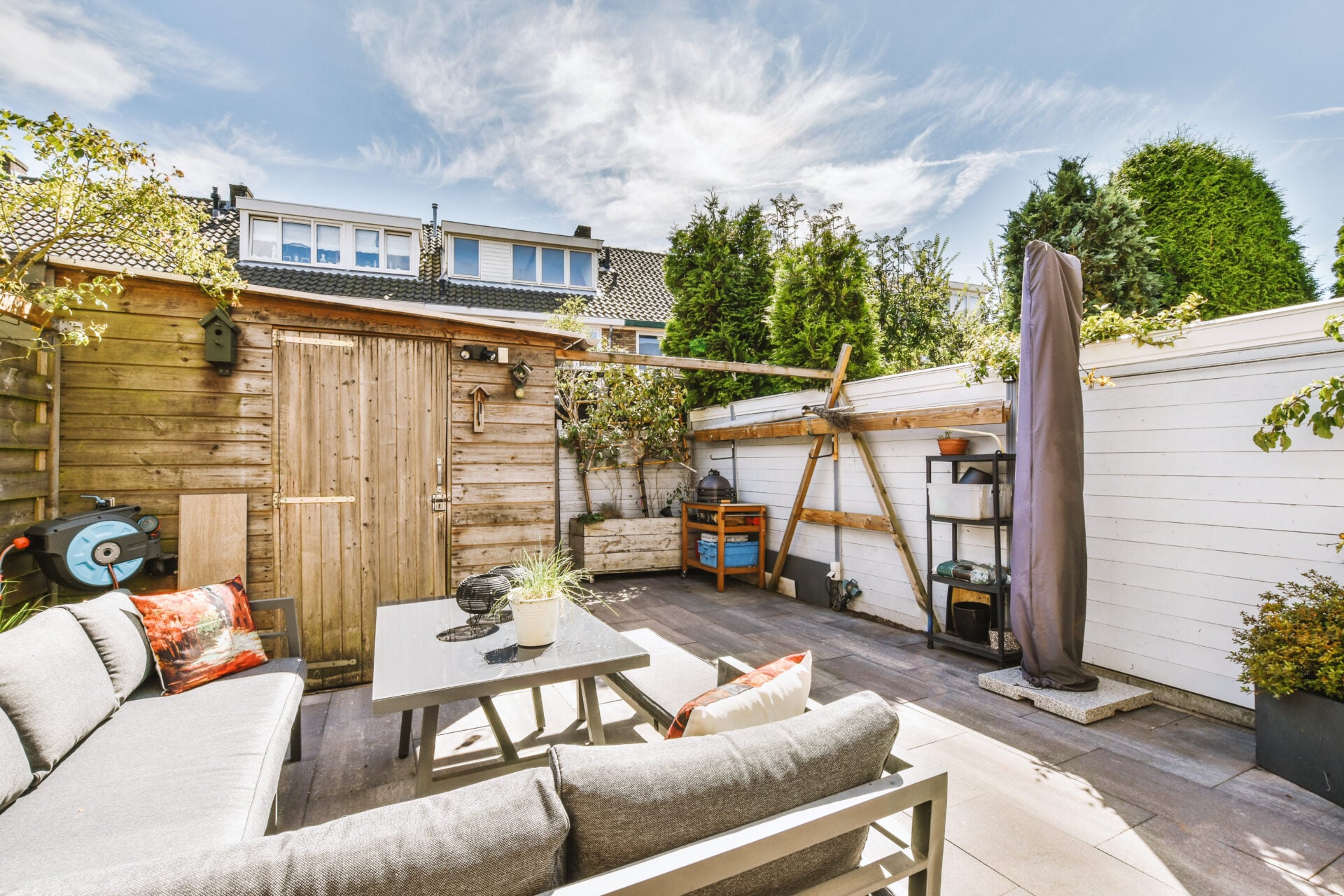 Neat paved patio with sitting area and small garden near wooden fence