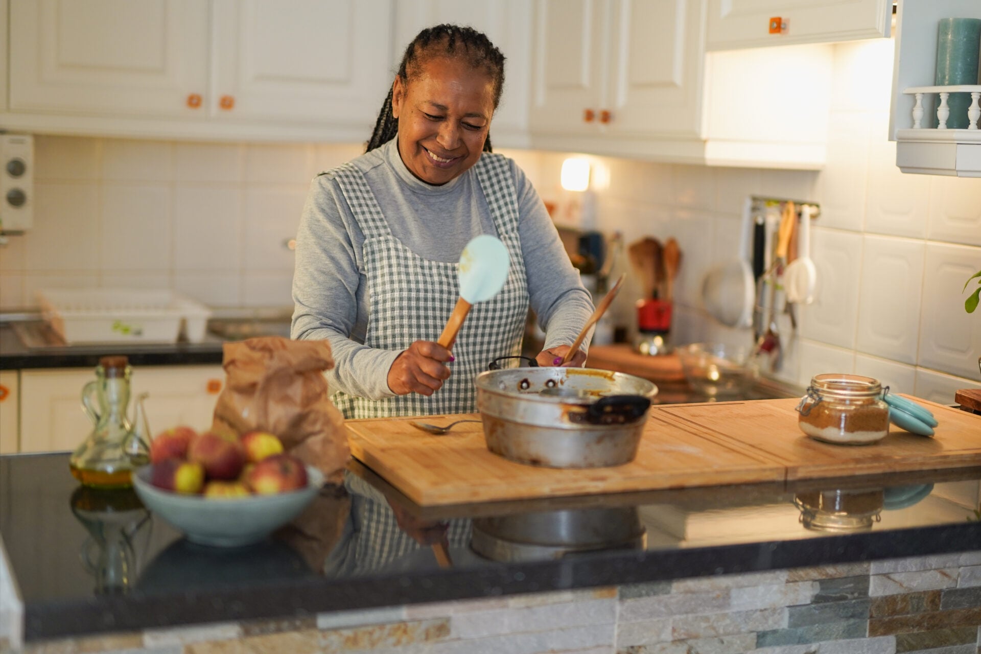 Happy senior woman dancing while preparing a cake at home - Joyful elderly african lady in the kitchen - Food, happiness and lifestyle concept