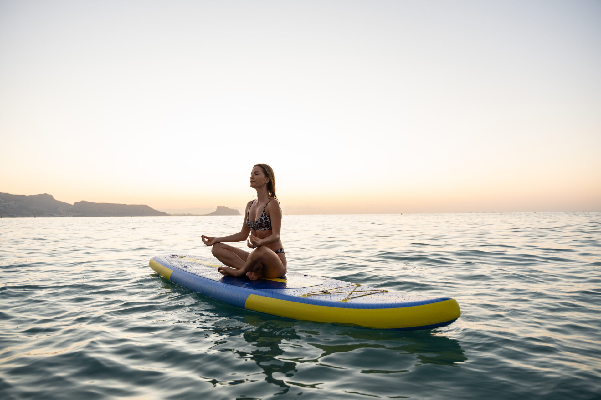 A millennial meditating on a surfboard on water